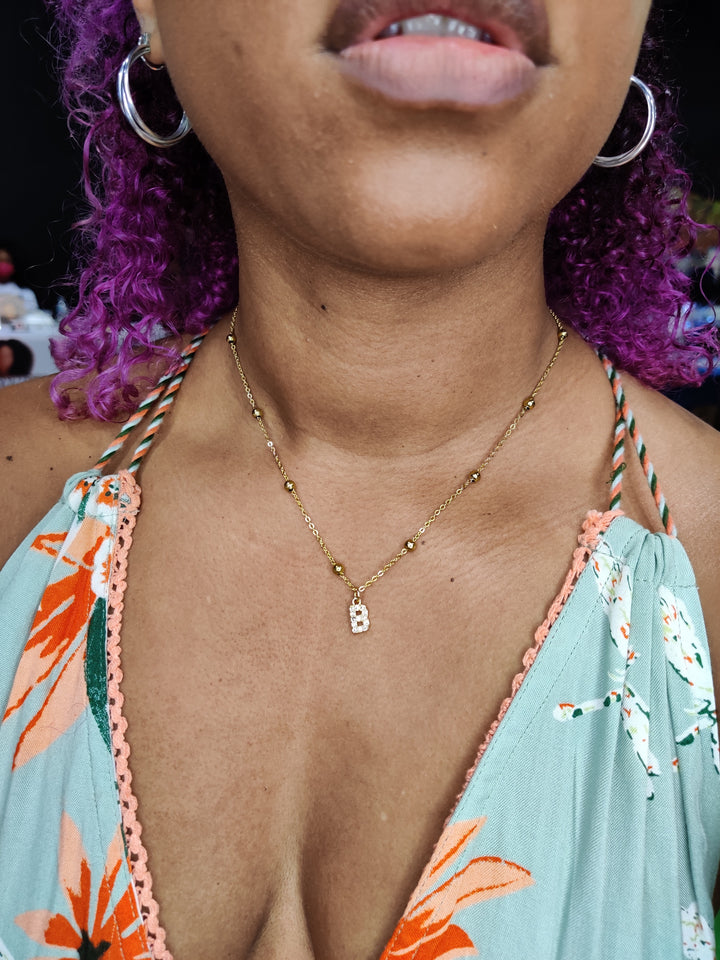 Close-up of a person wearing a Initial necklace that  is gold with a B along with a colorful dress with floral patterns.