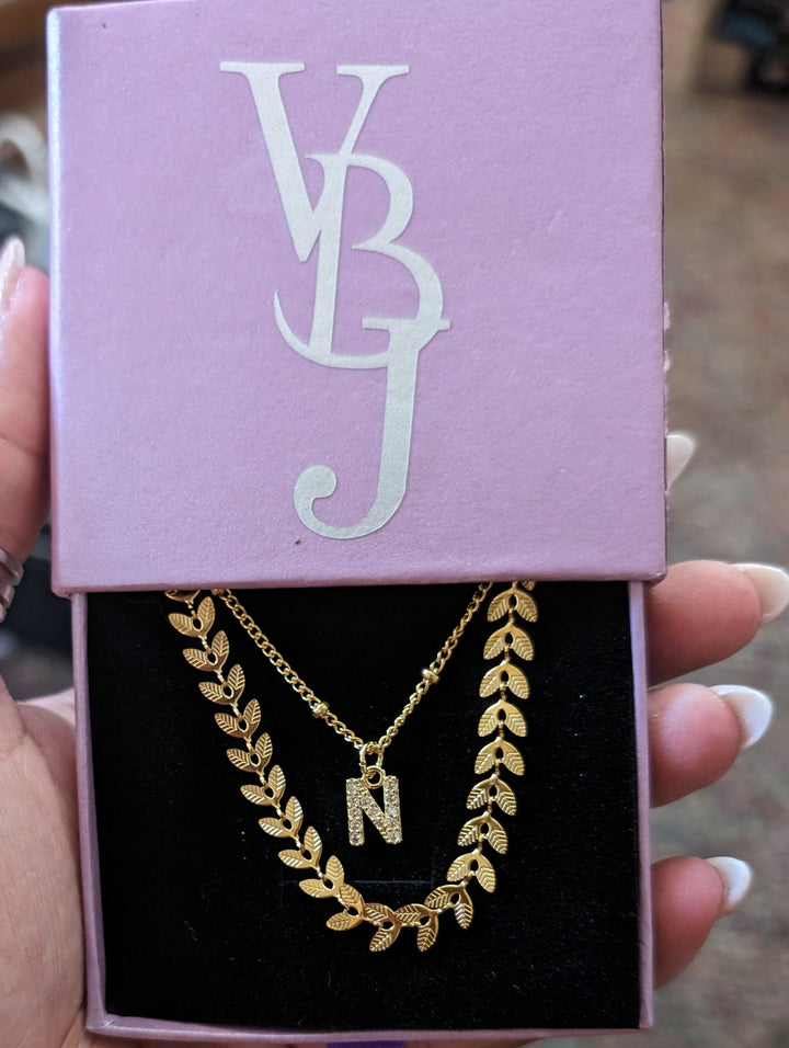 Gold necklace with 'N' pendant in a box with 'VB' initials held by a hand.