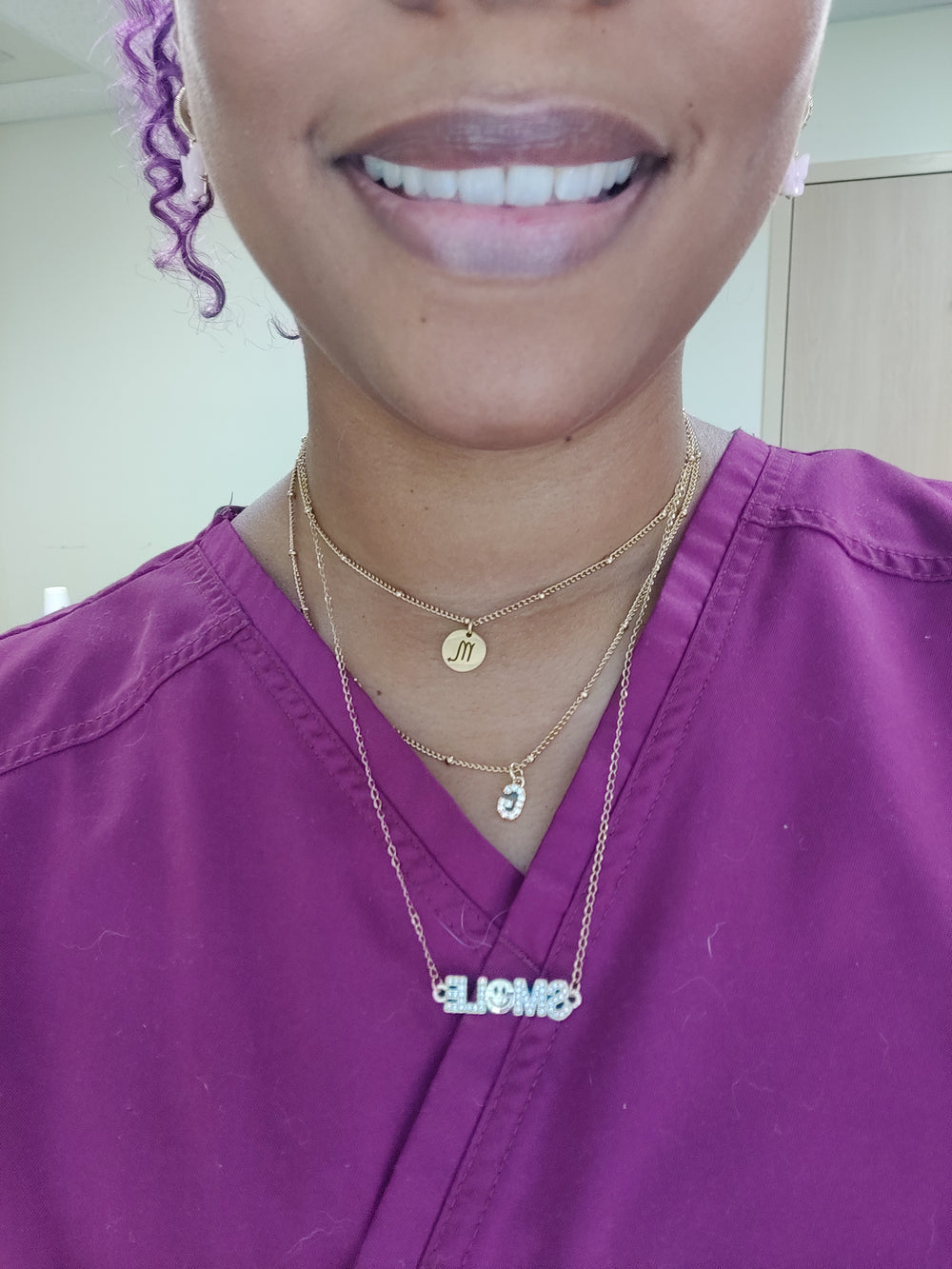 Person wearing a gold necklace with a small pendant, smiling.